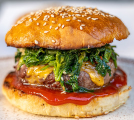cheeseburger with beef patty, spinach, red sauce, cheddar cheese piled up in a self-made bun