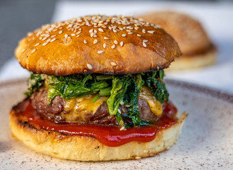 cheeseburger with beef patty, spinach, red sauce, cheddar cheese piled up in a self-made bun