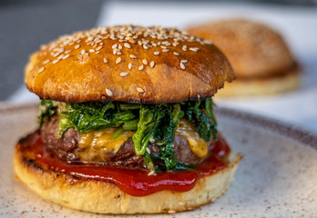 cheeseburger with beef patty, spinach, red sauce, cheddar cheese piled up in a self-made bun