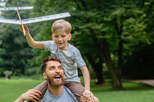 Happy cheerful family single american beard dad and child boy play laugh together, funny kid son holding toy plane having fun piggyback rides on summer park outdoor. Family vacation activity concept.