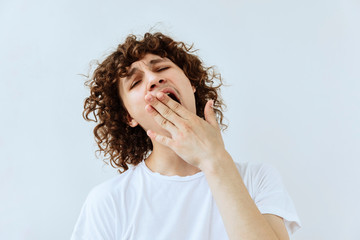 Tired,boredom and exhausted emotion. Yawning Curly teen guy portrait against white background