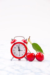 Time for cherry fruits. Red  clock with fresh red cherries on the marble table.