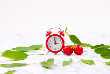 Time for cherry fruits. Red  clock with fresh red cherries on the marble table.