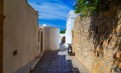 Fototapeta na wymiar Narrow street in Lindos town on Rhodes island, Dodecanese, Greece. Beautiful scenic old ancient white houses with flowers. Famous tourist destination in Europe
