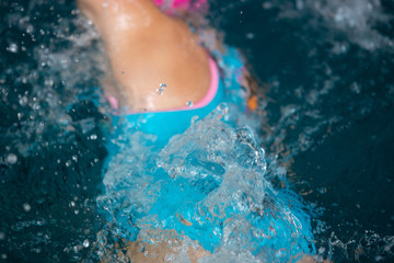Unidentified girl swimming under water in a blue swimming pool. Abstract image with wavy pattern of sunlight on the rippling water. Top view, intense colors.