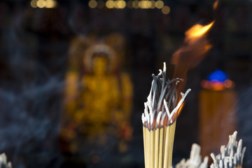 Burning incense sticks with out of focus Buddha statue in the background.