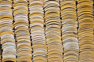 Stacks of yellow ceramic glazed curved roof tiles in a symmetrical pattern.