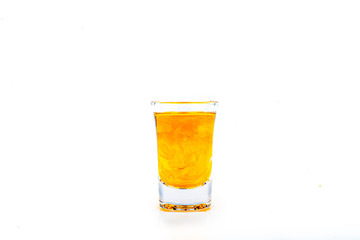 Orange food coloring diffuse in water inside shot glass with empty copyspace area for slogan or advertising text message, over isolated white background.