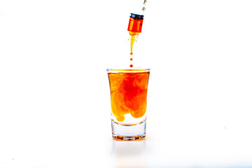 Orange food coloring diffuse in water inside shot glass with empty copyspace area for slogan or advertising text message, over isolated white background.