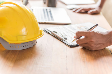 Architect engineer using laptop for working with yellow helmet on desk.