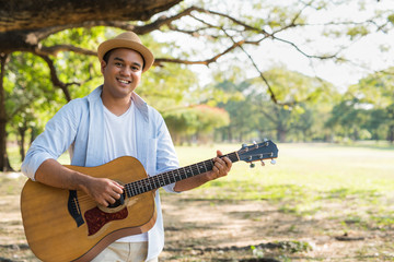 Young asian man playing guitar in park