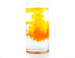 Orange food coloring diffuse in water inside tall glass with empty copyspace area for slogan or advertising text message, over isolated white background.