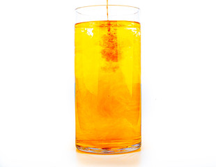 Orange food coloring diffuse in water inside tall glass with empty copyspace area for slogan or advertising text message, over isolated white background.