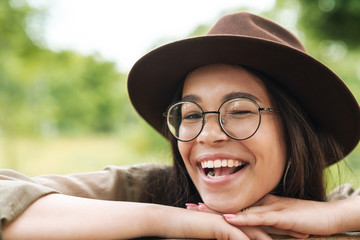 Photo closeup of young woman wearing hat and eyeglasses smiling with open mouth and winking while...