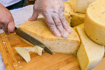 Man cuts the cheese on a wooden board. Closeup of slicing cheese. A man cuts thin slices of cheese. On the table are different types of cheese. Sale and tasting of dairy products