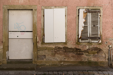 Fassade von verlassenem, vernageltem, baufälligem Haus mit Tür und 2 Fenstern mit Fensterläden
