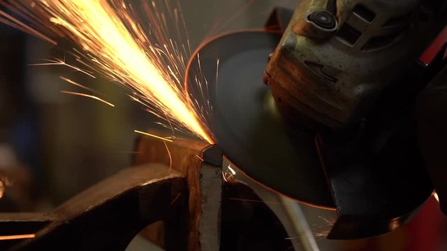 Slow motion closeup of sparks flying from a disc grinder as it is used to cut a heavy piece of steel held in a vice.