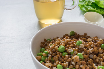 The concept of healthy food. Vegetarian breakfast. Bowl with spelled wheat and green peas, cucumbers, lettuce leaves, cup on gray background.
