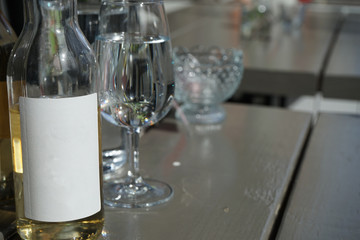 Clear cider bottle with with label on with glasses in the background.