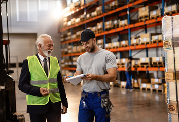 Happy worker and senior businessman reading reports in factory warehouse.