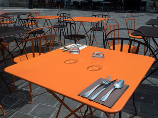 A bright orange table part of black and orange furniture in an outdoor street restaurant is has place settings for two people.Saumur in France - Image