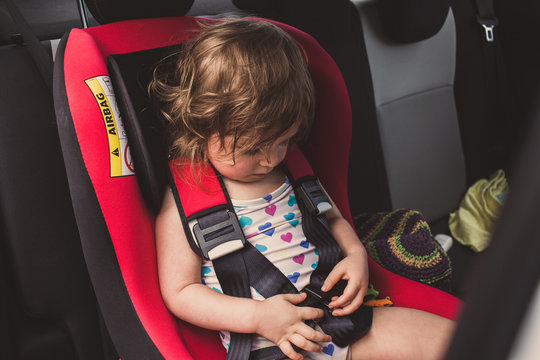 Baby toddler girl securing herself in car seat in car. Holiday rental car, summer, vacation by car with kid, safety