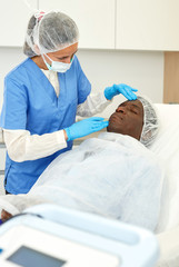 Female doctor examining skin of patient before facial procedure in clinic