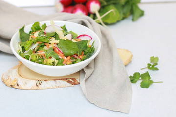 Fresh vegetable salad with greens and radishes, carrots and spinach leaves. Beautiful salad serving on the table, on a wooden stand in rustic style. Сoncept of healthy food, organic food, vegetarian