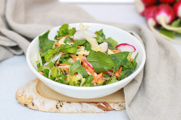 Fresh vegetable salad with greens and radishes, carrots and spinach leaves. Beautiful salad serving on the table, on a wooden stand in rustic style. Сoncept of healthy food, organic food, vegetarian