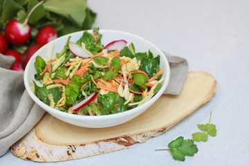 Fresh vegetable salad with greens and radishes, carrots and spinach leaves. Beautiful salad serving on the table, on a wooden stand in rustic style. Сoncept of healthy food, organic food, vegetarian