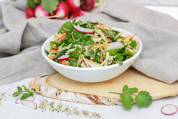 Fresh vegetable salad with greens and radishes, carrots and spinach leaves. Beautiful salad serving on the table, on a wooden stand in rustic style. Сoncept of healthy food, organic food, vegetarian