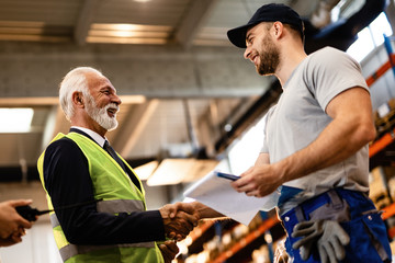 Below view of happy mature manager shaking hands with a worker in industrial building.