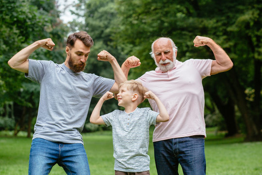 Portrait og happy family - grandpa, father and his son smiling and showing their muscles outdoor in park on background. Three different generation concept.