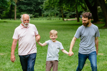 Portrait og happy family - grandpa, father and his son smiling walking together outdoor in park on...