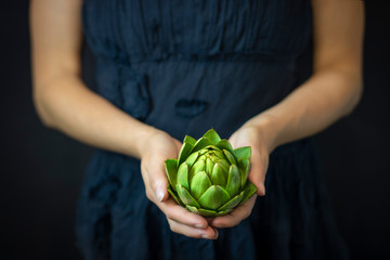 Woman is holding the artichoke on black background. Artichokes close-up. Healthy food concept,...
