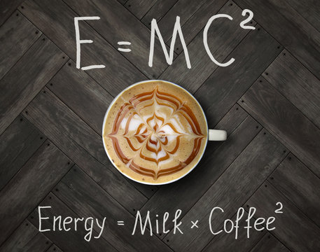 The cup of black energy coffee with milk and two funny formulas. Wooden background.