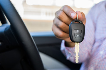 Close up male hand showing car key while sitting in car.