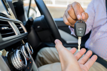 Businessman giving a car key while sitting in car. Getting new car concept.