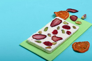 Homemade white chocolate. Decorated with slices of dried orange, strawberries, cherries and pistachios. It lies on a light green napkin on a mint background.