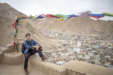 Asia traveler man enjoy with traditional Tibetans Prayer flag in difference five color flags with background of Leh Ladakh city and Himalaya mountain in north of India.