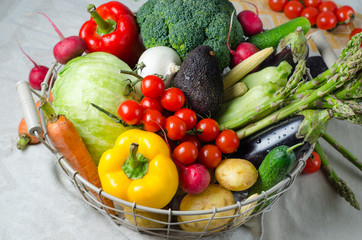 Fresh vegetables in a metal basket on the table. Cherry tomatoes, asparagus, broccoli, potato, peppers, radish, eggplants, zucchini, carrots and onions.