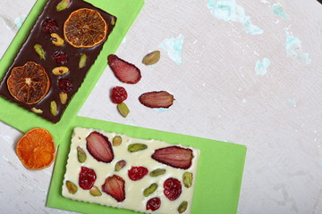 Naklejka na ściany i meble Homemade white and black chocolate. Decorated with slices of dried orange, strawberries, cherries and pistachios. On an aged surface with peeling paint.