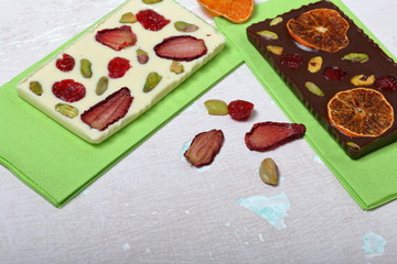 Homemade white and black chocolate. Decorated with slices of dried orange, strawberries, cherries and pistachios. On an aged surface with peeling paint.