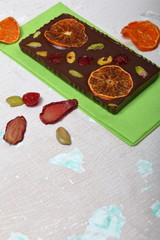 Homemade black chocolate. Decorated with slices of dried orange, strawberries, cherries and pistachios. On an aged surface with peeling paint.
