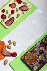 Homemade white and black chocolate. Decorated with slices of dried orange, strawberries, cherries and pistachios. On an aged surface with peeling paint.