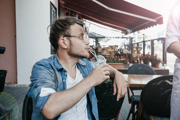 young hipster male in a summer cafe on the terrace in sunglasses