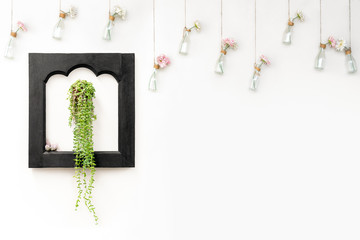 Ivy in black wooden frame on white wall with flowers in hanging bottles.