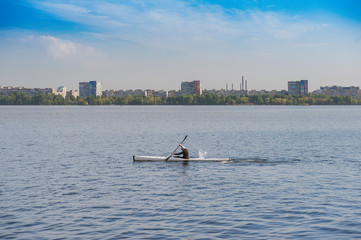 Header for the site. Panoramic view. Wide calm lake and oarsman in sport boat with city landscape on background