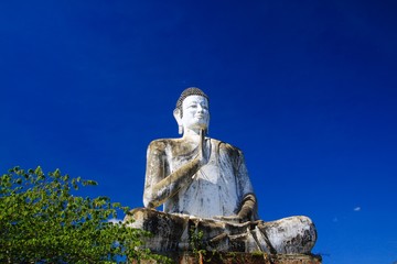 Big white Buddha statue raising high contrasting with blue cloudless sky at Wat Ek Phnom, near Battambang, Cambodia