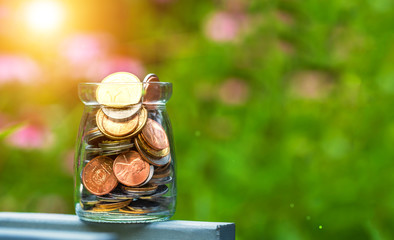 Conceptual image of saving money. Bottle of coins with nature background
